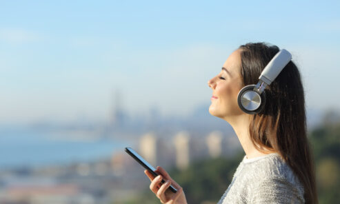 image of a lady holding a phone with headphones on, listening to the Spinnaker audio stories